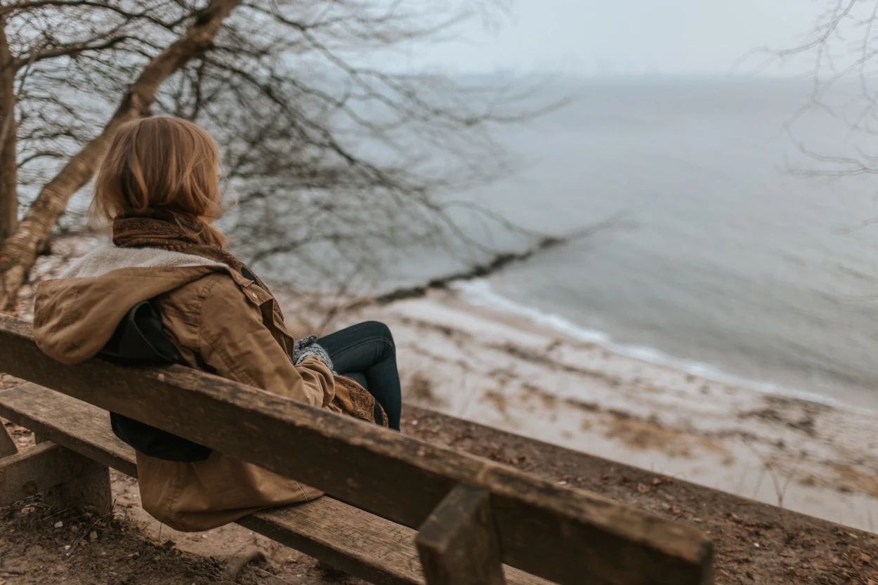 A woman sitting on bench looking at a lake
