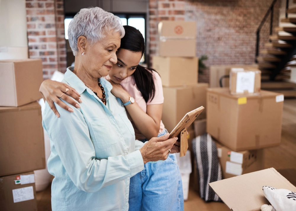 Two women looking at a picture frame, surrounded by moving boxes.